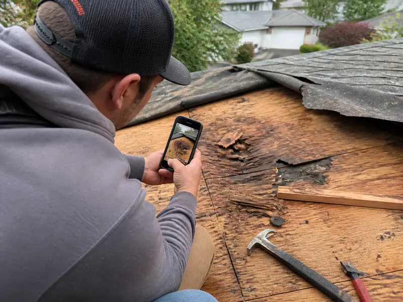 Roofer photographing rotted decking during tear off for an insurance supplement roofing claim