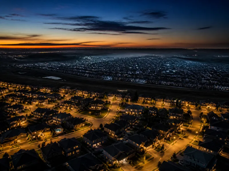 Aerial view of a fully claimed neighborhood beside a distant, unclaimed roofing market at dusk