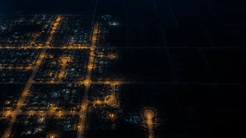 Aerial view of a suburban neighborhood grid at night, with some blocks lit in warm amber and others fading into darkness