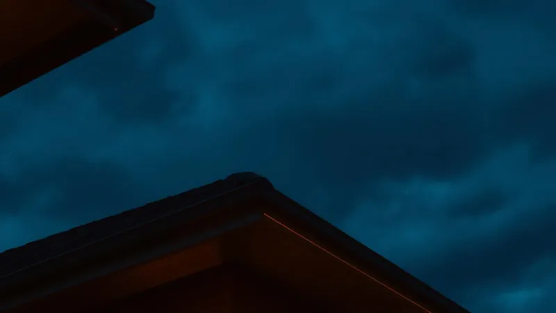 Dusk rooftop silhouette with warm amber eave light, evoking a roofing company's after-hours reputation